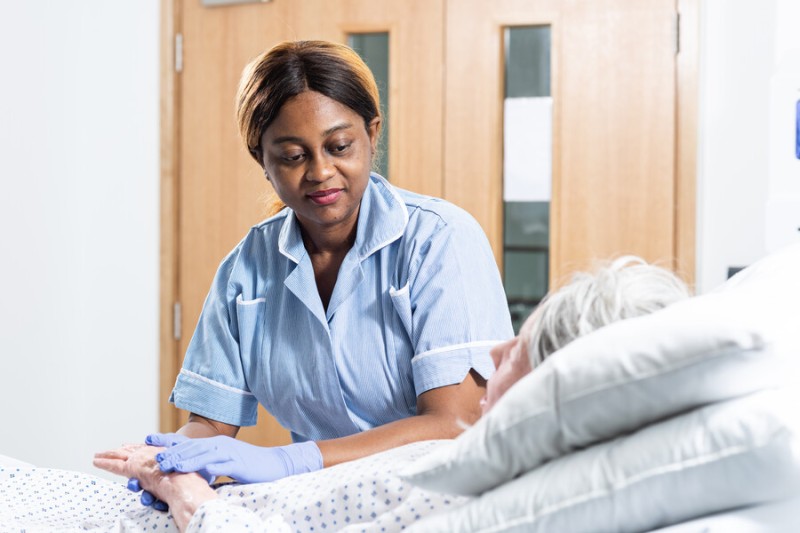Student nurse tends to an elderly patient in bed