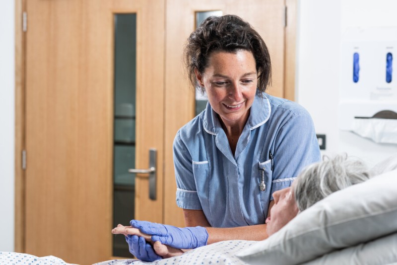 Student nurse tends to an elderly patient in bed