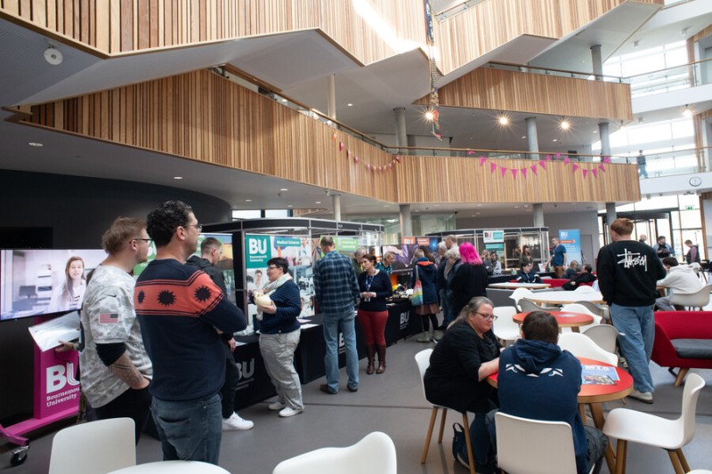 Inside the Fusion building with stalls, banners and people sitting or looking at stands