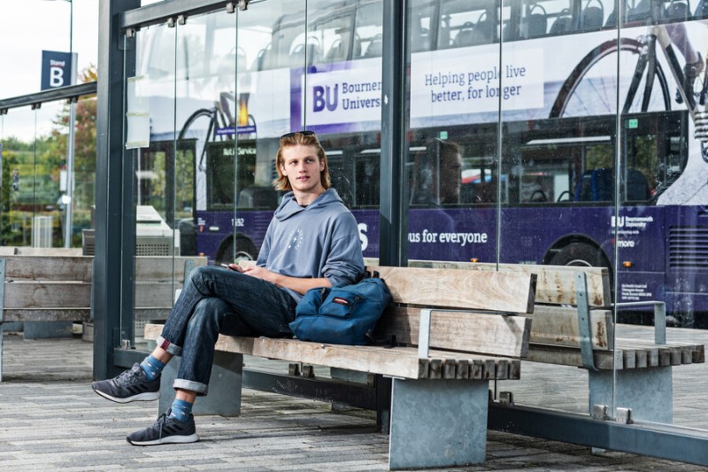 Student sitting at a bus stop with a BU bus behind him