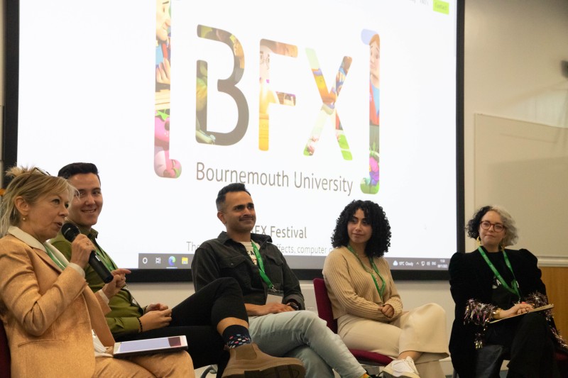 Three women and two men sitting on a stage addressing the audience. The BFX logo is on the big screen behind them