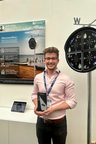 Zander holding up his award in front of a poster with a picture of fishers on a lake and text explaining how his product works