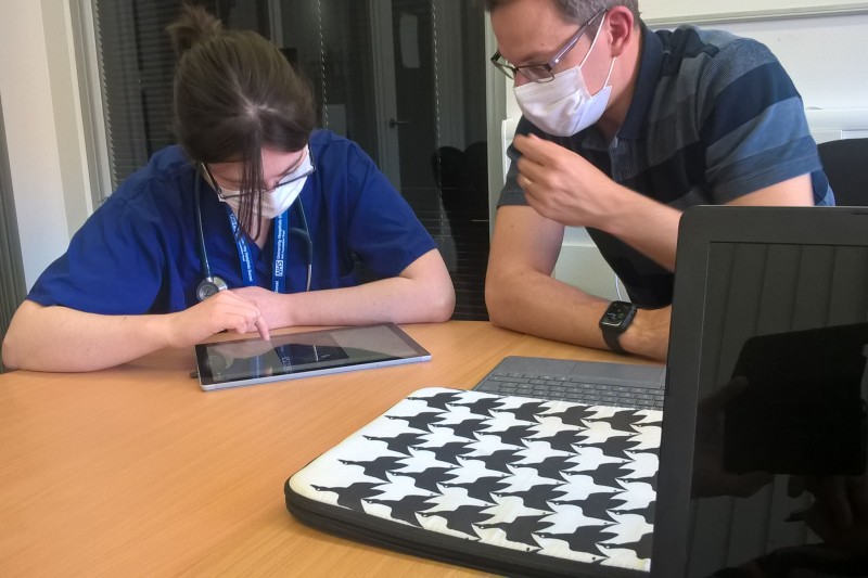 Two doctors sat at a desk with an iPad, testing the Admission game