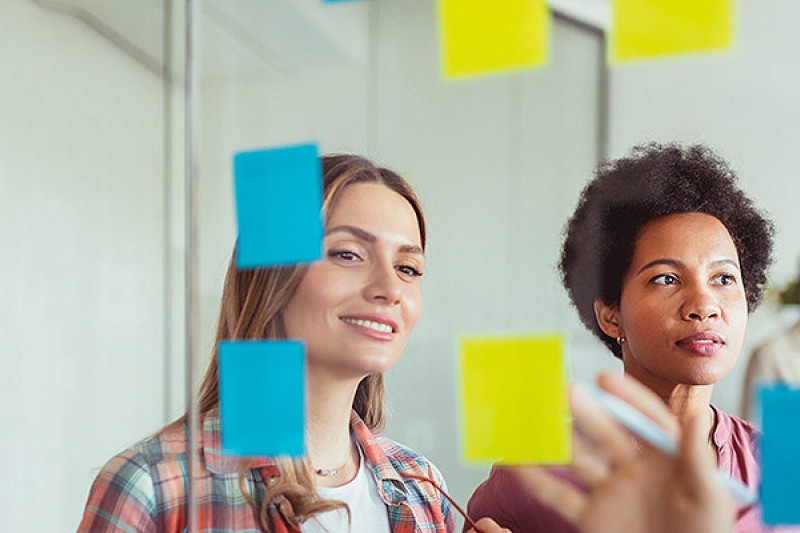 Three people looking at a  clear screen with stuck post-it notes