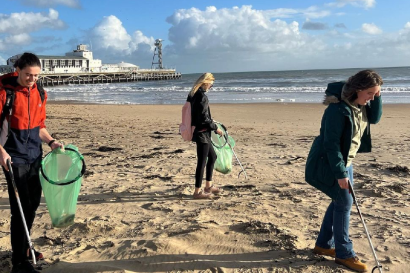 Three people on the beach picking up litter with Bournemouth Pier behind them