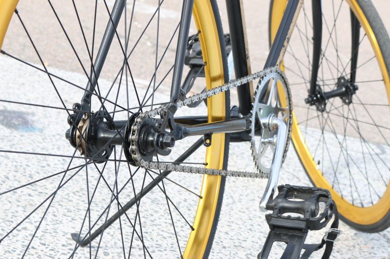 Close up of the pedals, gears and wheels of a black and yellow bike