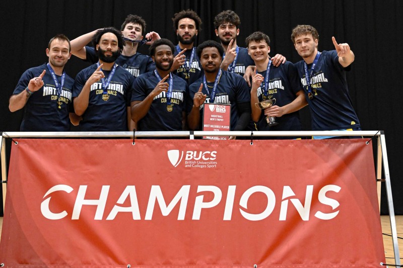 Nine players in their basketball kit in front of a banner saying "champions"