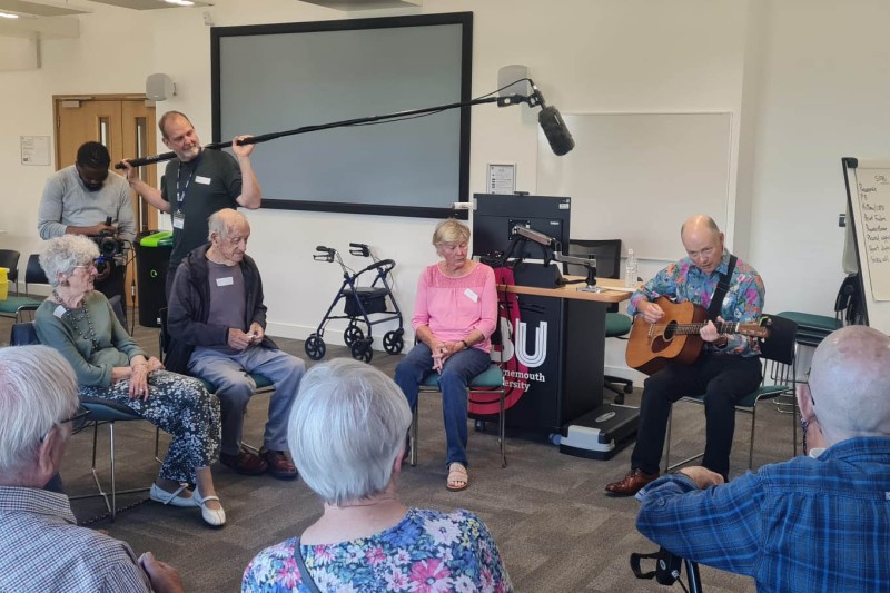A group sat in a circle with a man playing guitar