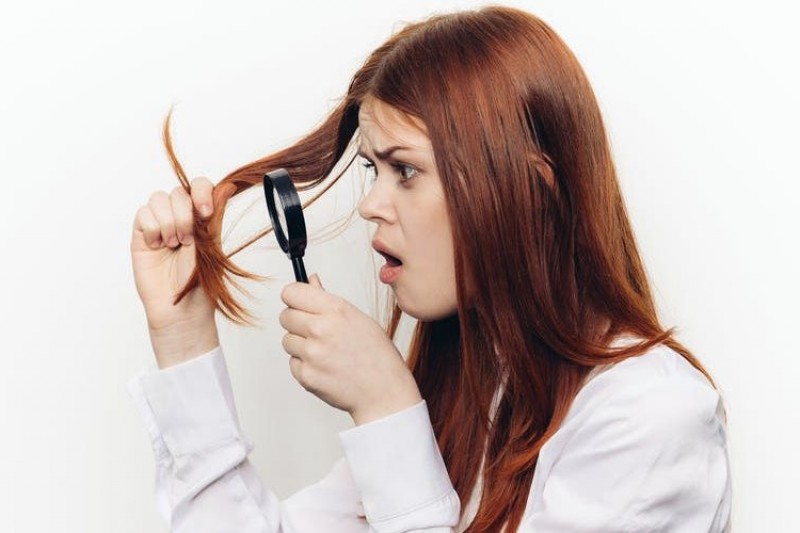 A woman inspecting her hair with magnifying glass
