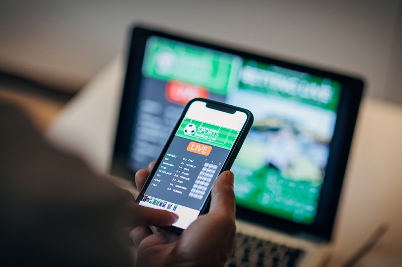 A photo of a mobile phone and a laptop, both of which are showing online gambling pages