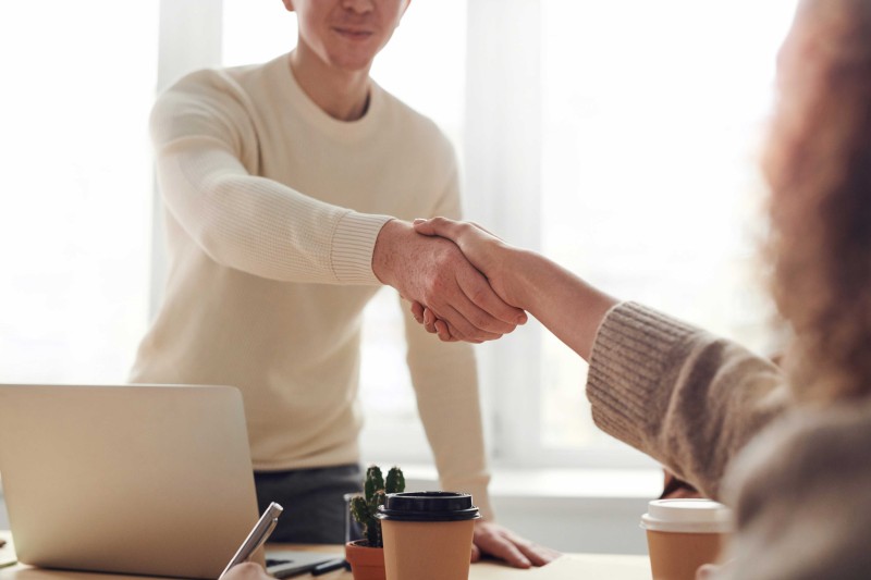 A young man standing up shakes hands with a woman over a desk 