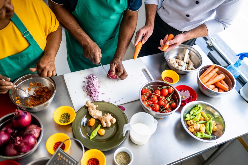 An aerial shot of hands preparing food, with bowls of fruit and vegetables on the table