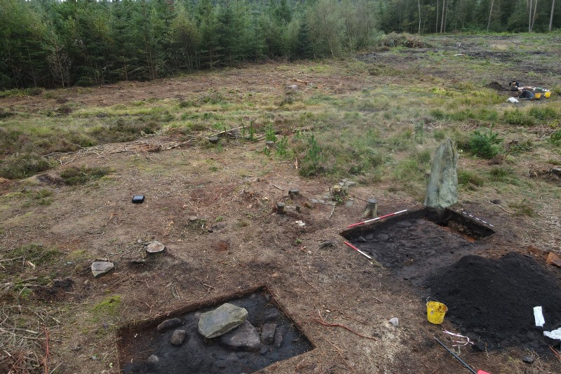 A picture of he standing stone with two other large stones next to it in excavated ground