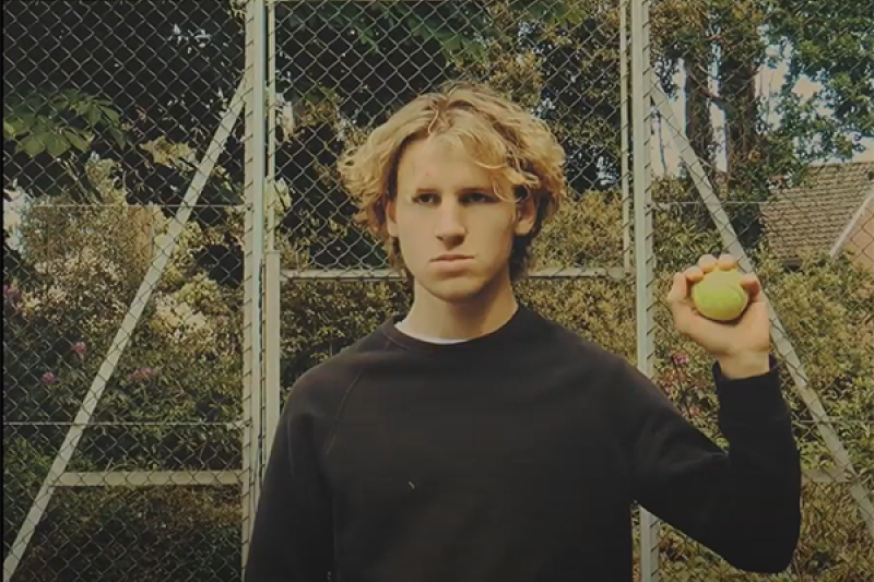 Young man with a stern, unimpressed face holds up a tennis ball which he caught to disrupt a tennis match