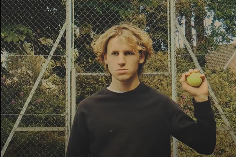 Meanest Man in Meyrick - tennis match Young man with a stern, unimpressed face holds up a tennis ball which he caught to disrupt a tennis match