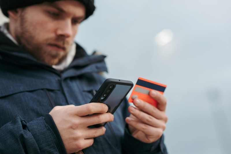 A man holds his phone in one hand a his credit card in the other, looking serious