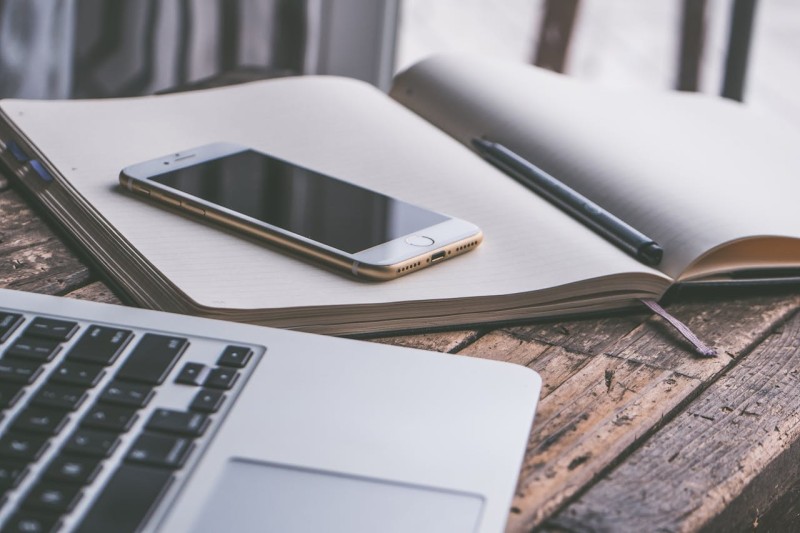 A laptop positioned next to a notepad with a phone on it A laptop positioned next to a notepad with a phone on it