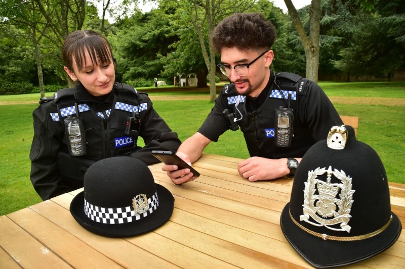 Two police officers sat at a picnic table using a mobile phone 