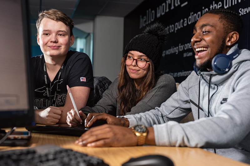 Three students working together on a project around a computer monitor