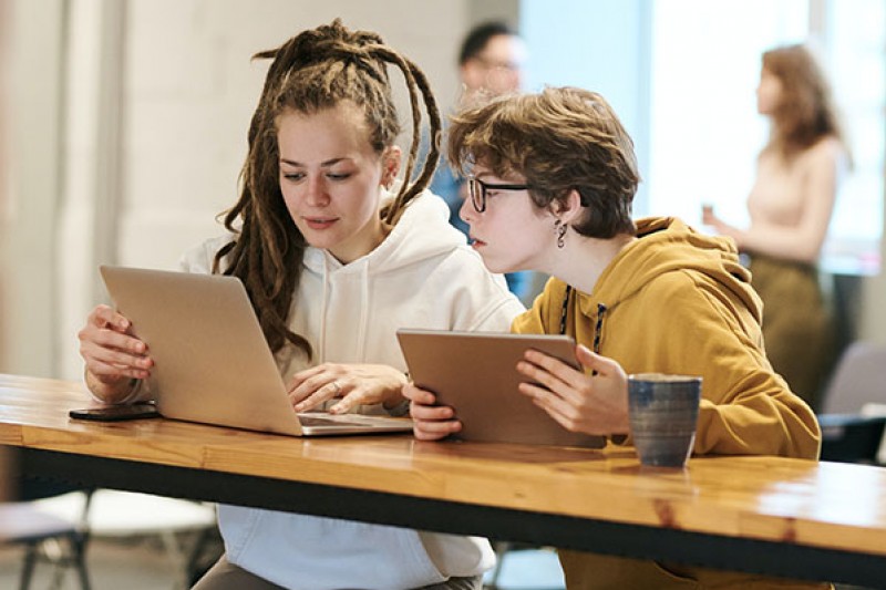 Two students watching laptop and tablet