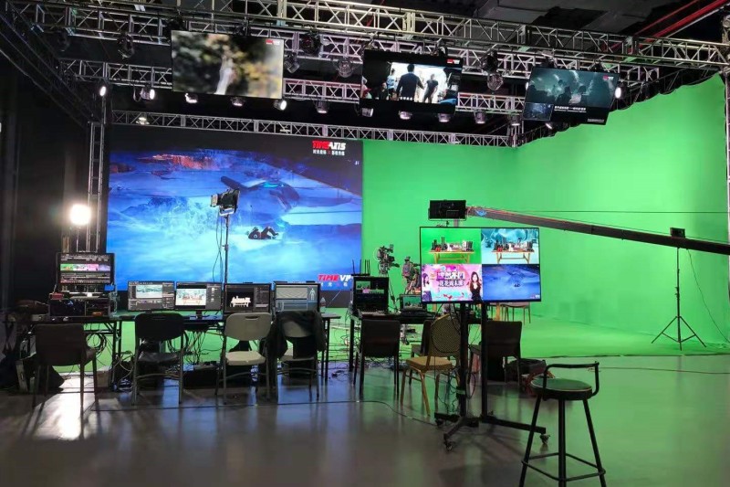 A green screen studio with computers and a large LED screen 