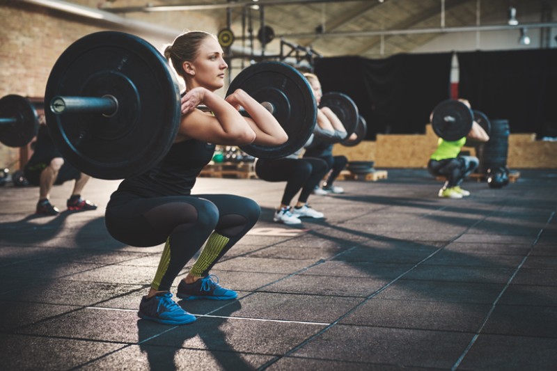 A weightlifting class with women and men squatting with large barbell weights before a lift